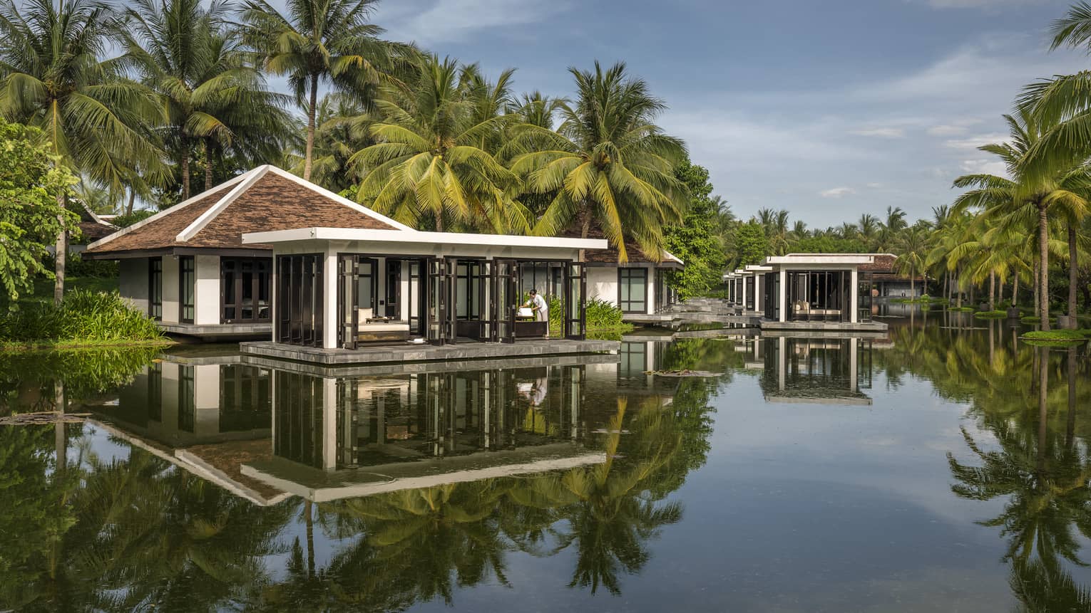 Overwater Heart of Earth spa villa staff folds white towels on deck, reflection in water