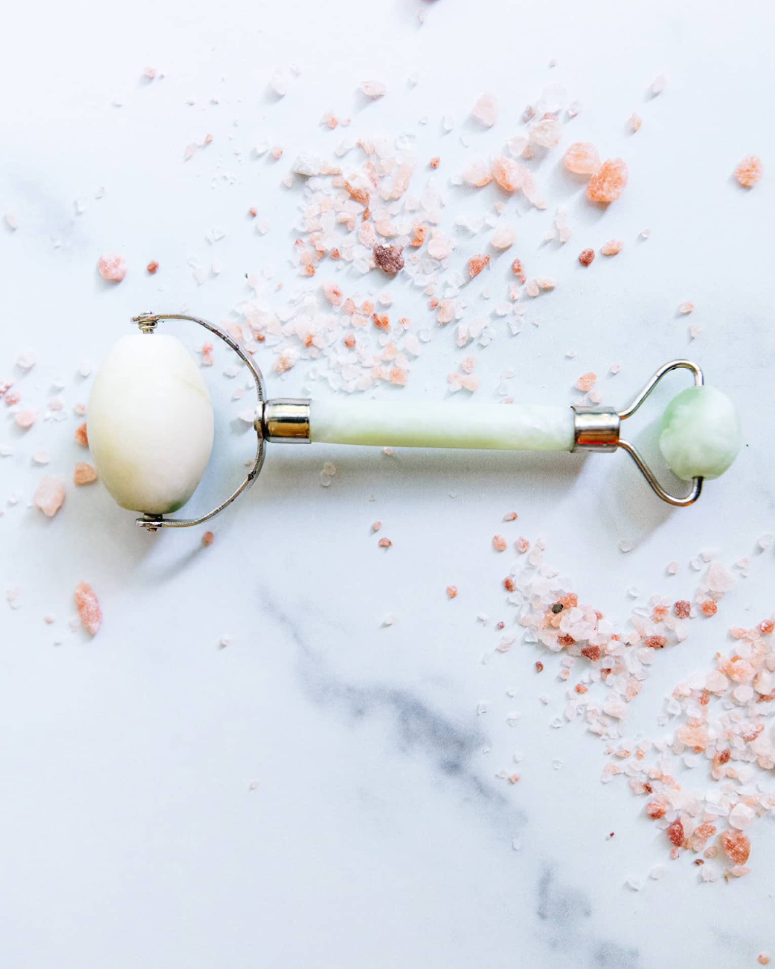 a spa roller tool on a white marble counter surrounded by himalayan salt