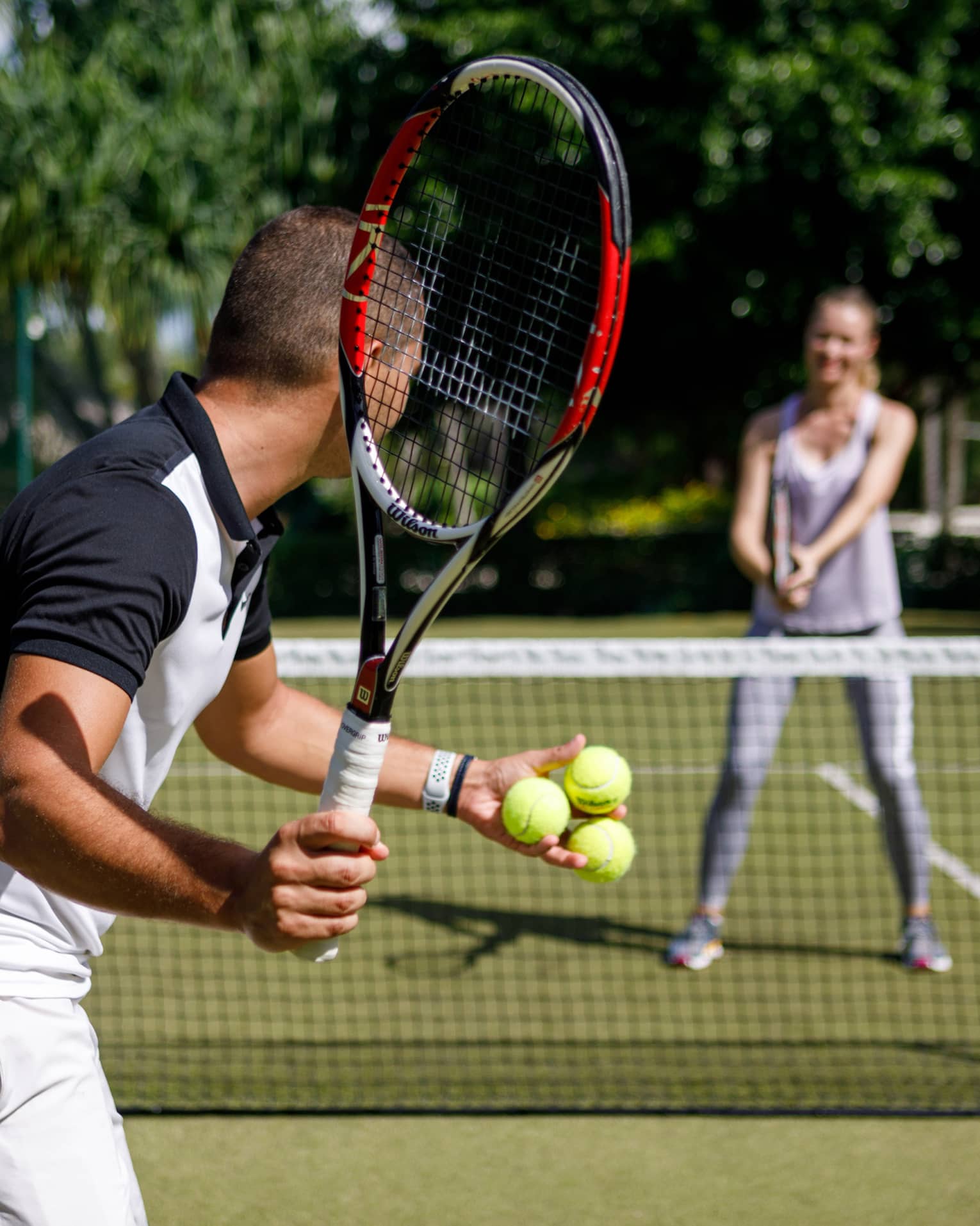 Couple playing tennis on court, man prepares to serve tennis balls to woman ready to swing