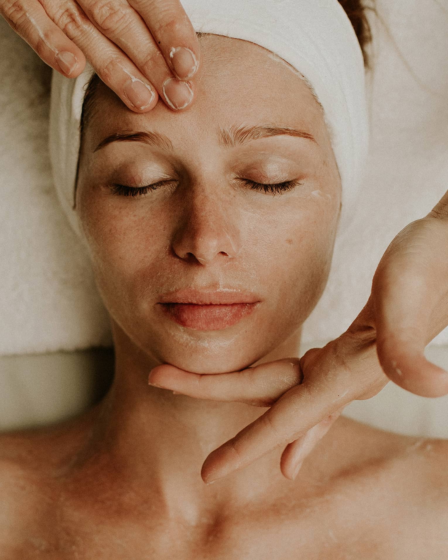 A woman reclines as a spa attendant performs a facial