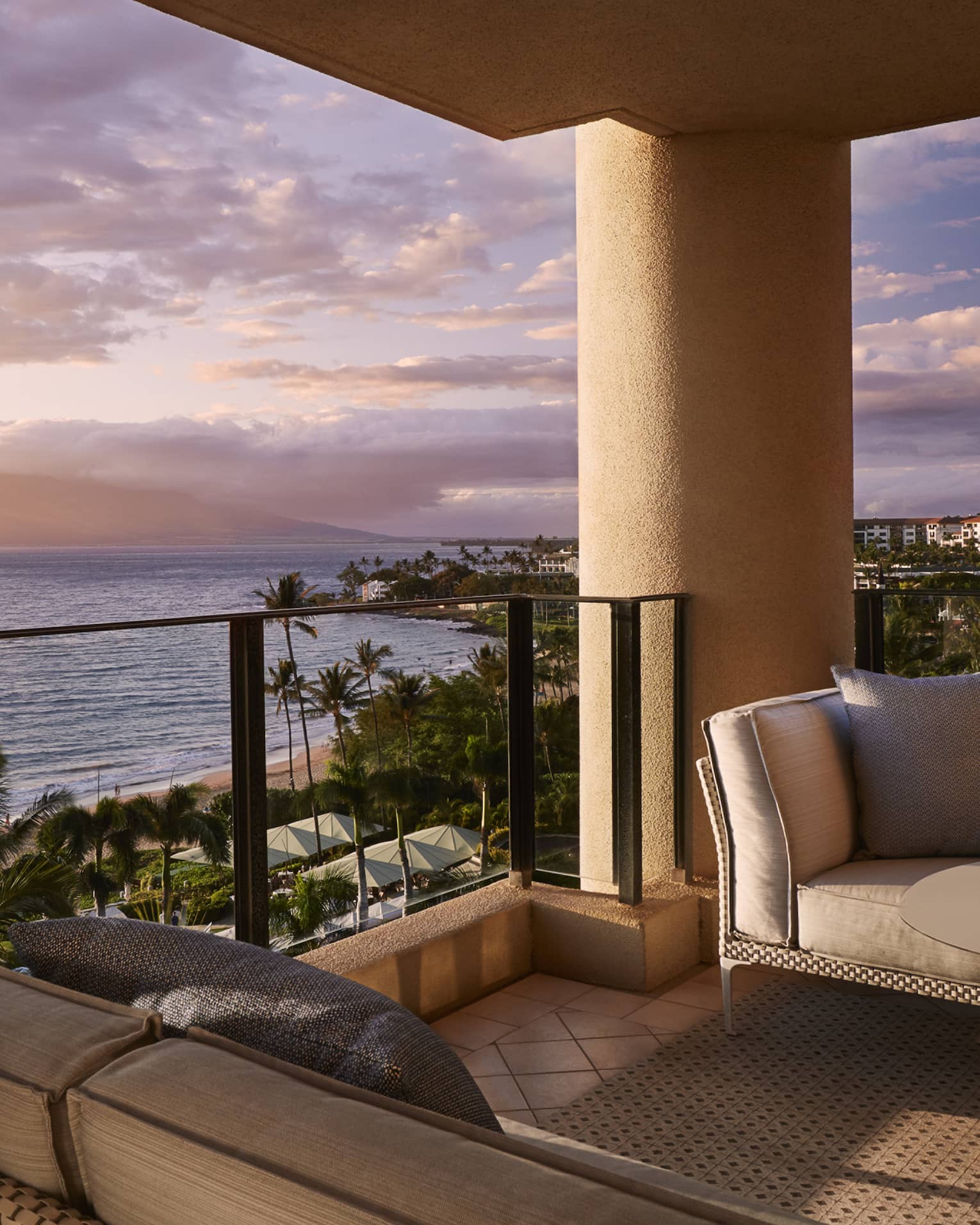 Balcony with wicker patio furniture, brown cushions in front of ocean view at sunset