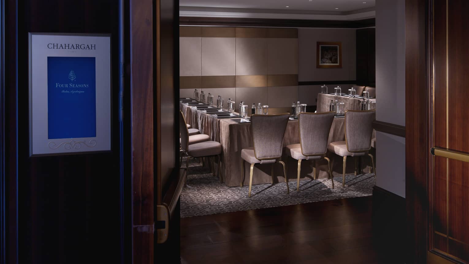 View through door to dimly-lit meeting room with modular table, chairs 