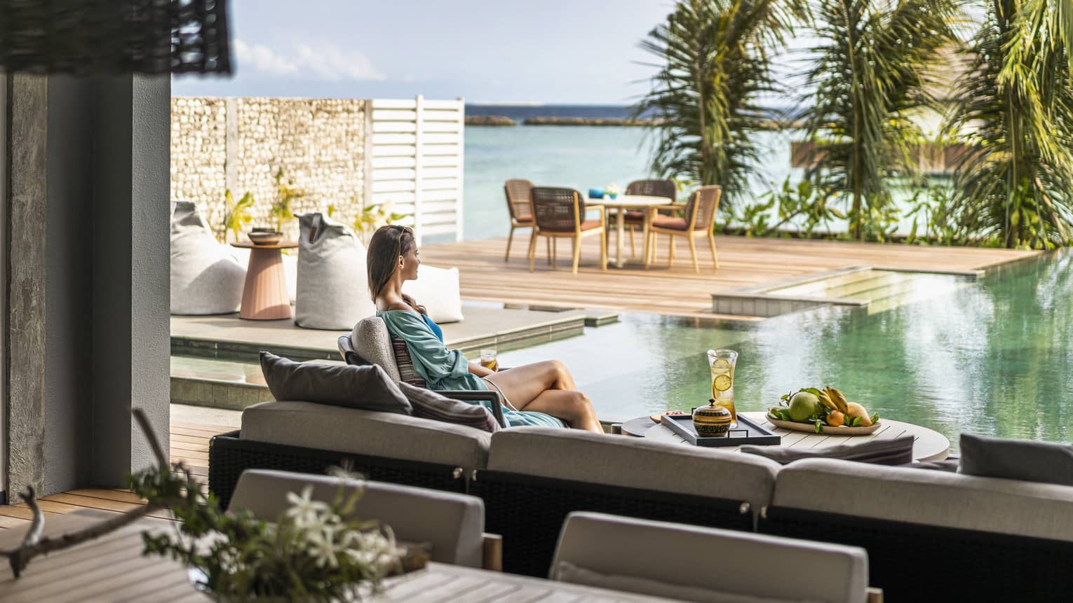 Woman lounges on outdoor terrace sofa next to pool and ocean