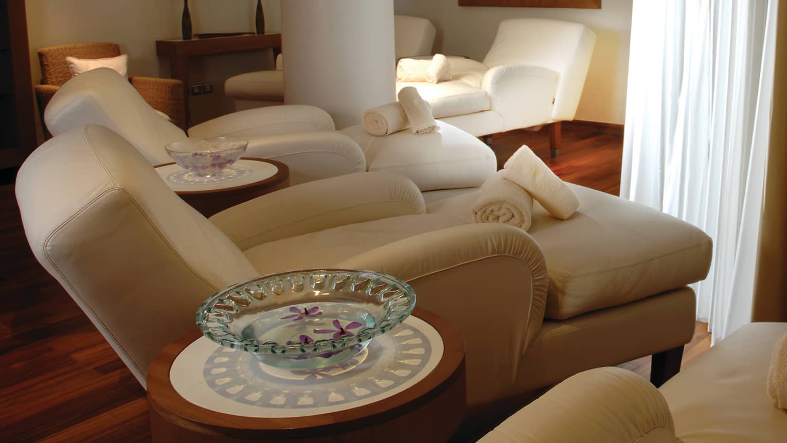 Three large plush chaise lounge sofas in dimly-lit spa room, rolled white towels
