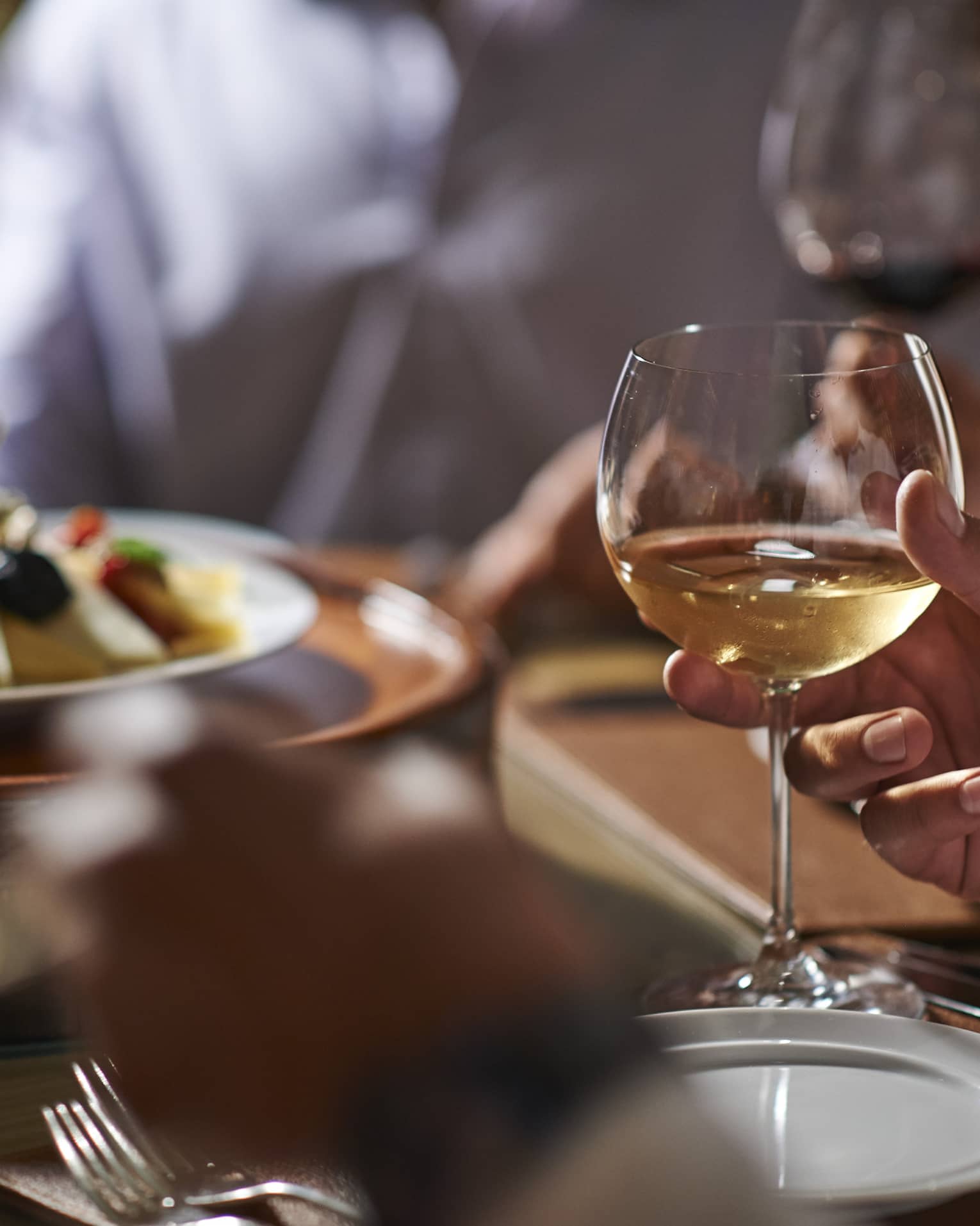 Close-up of hand holding wine glass by dinner plate on table