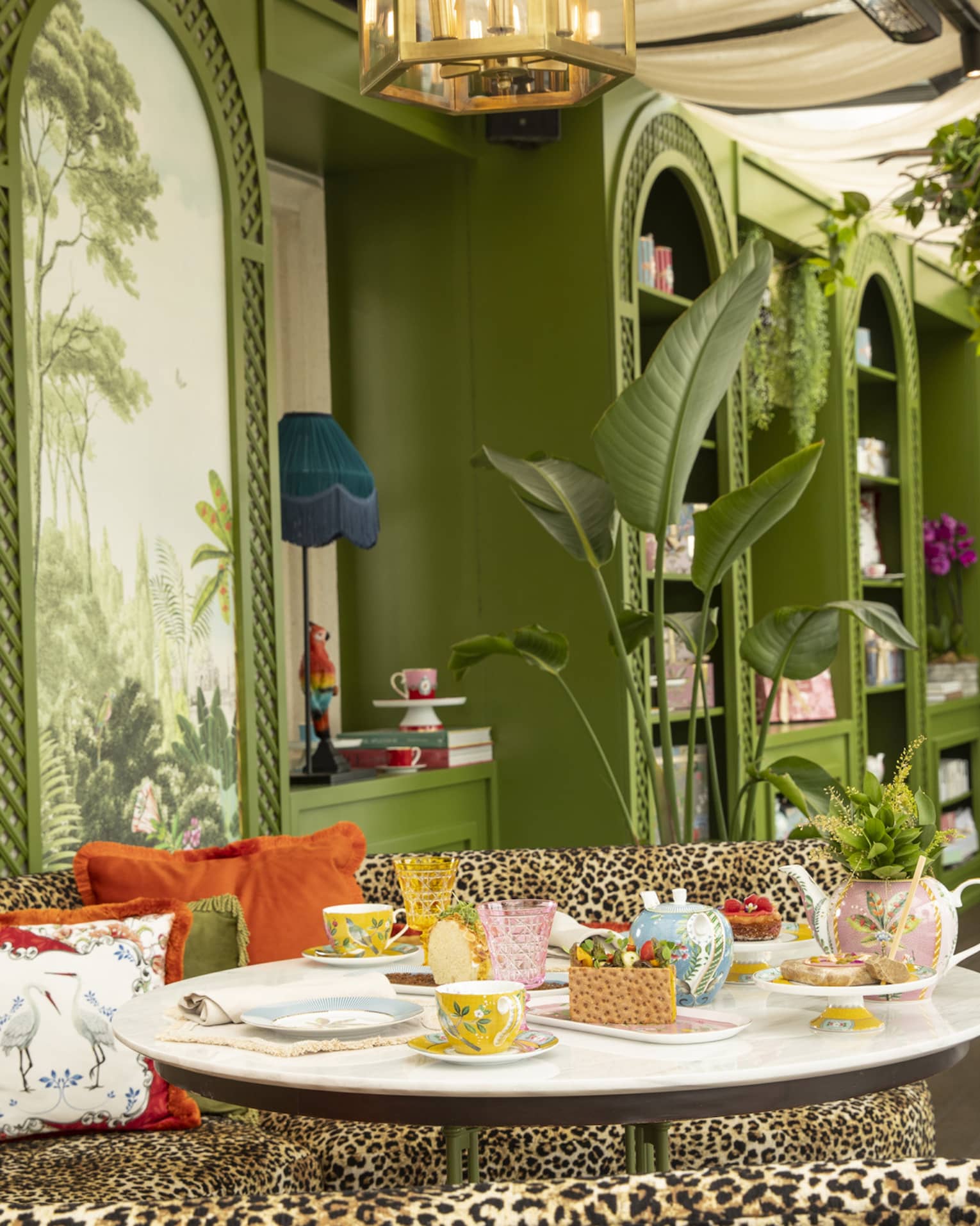 Gracebrands Patisserie setup by curved leopard-print couch topped with orange pillows and green walls in backdrop