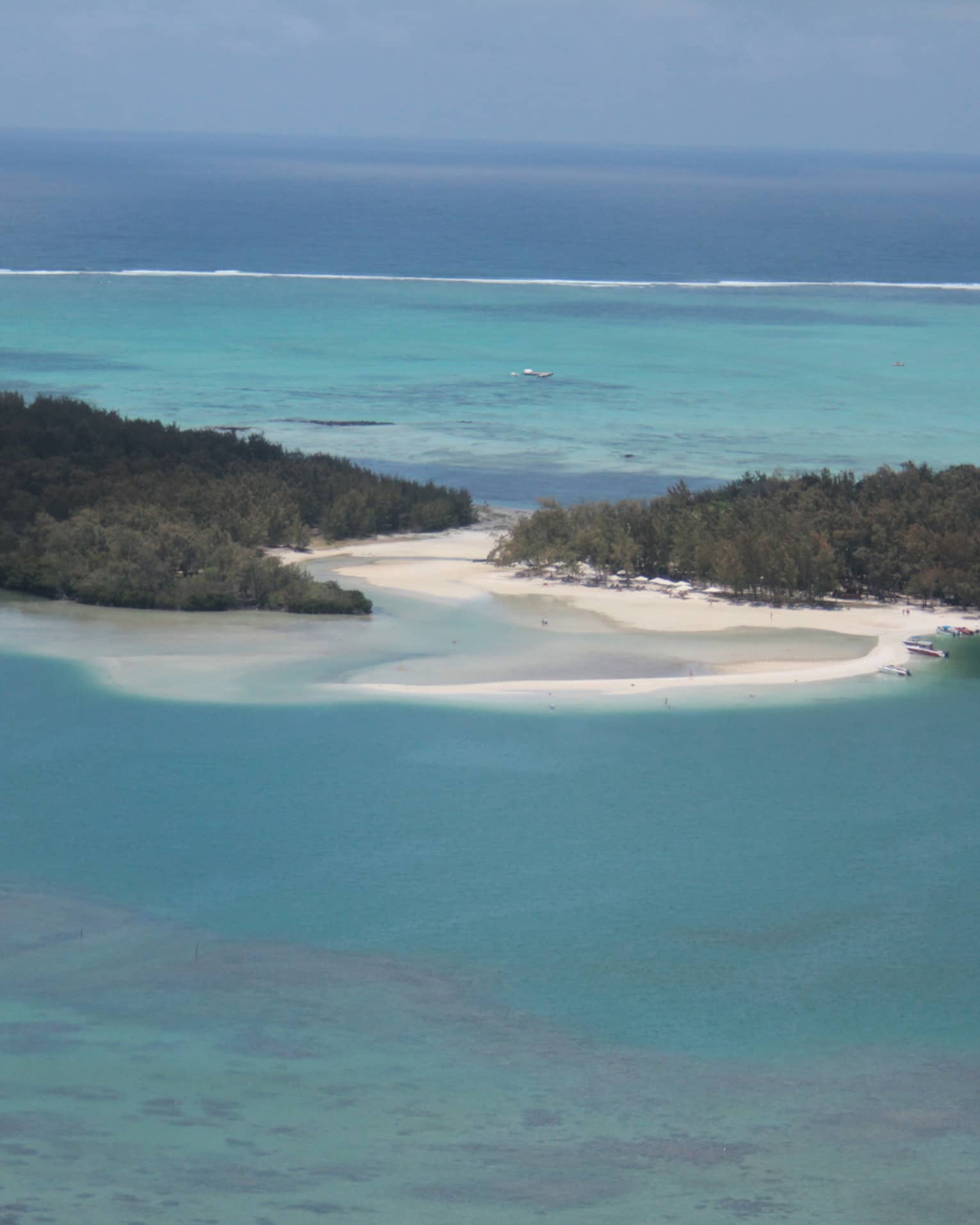 Two islands covered in lush forest separated by a white sandy beach, calm turquoise water receding toward a clear blue sky.