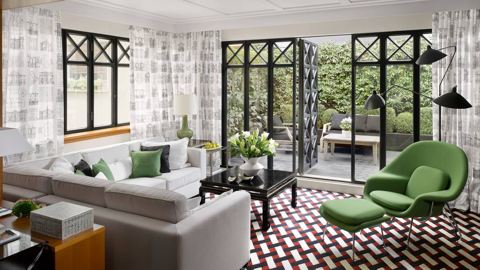 Fashion Suite grey, white sofas, green armchair on retro-style red-and-black tile floor, open balcony doors