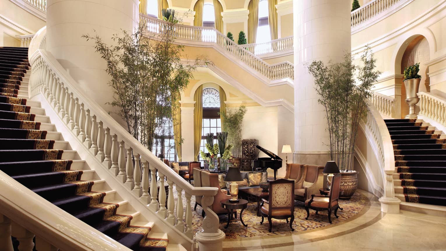 Hotel lobby with two grand staircases around large white pillars, seating area