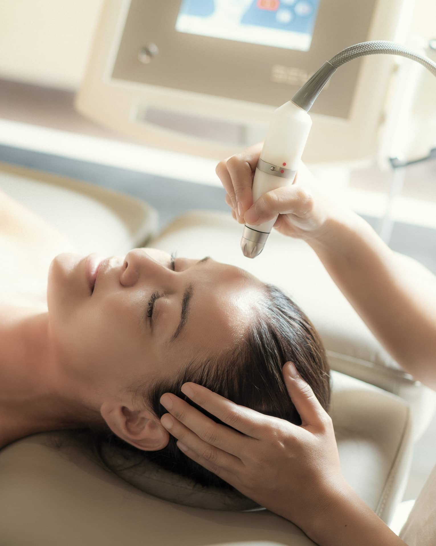 An aesthetician uses a tool on the face of a relaxing woman.