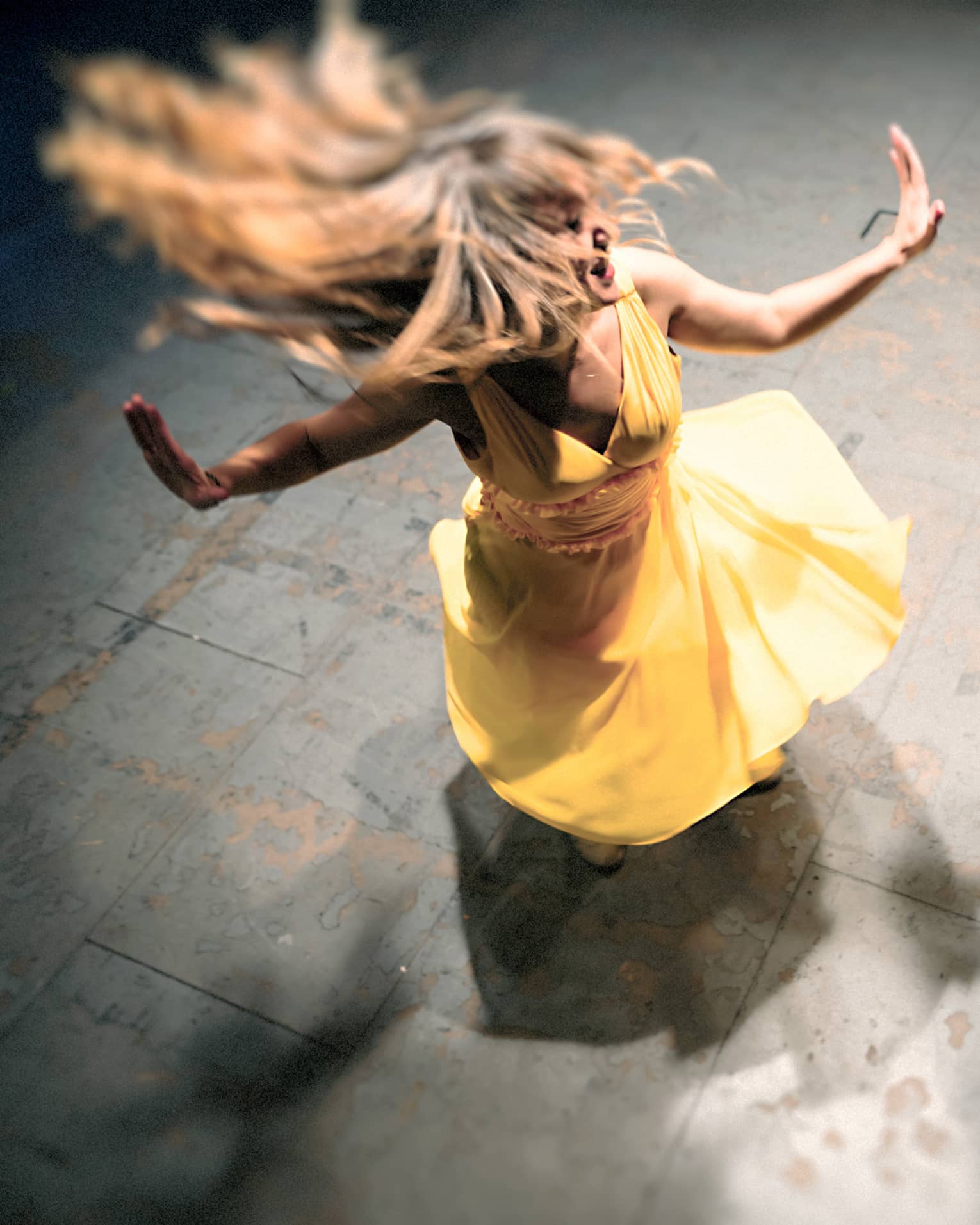 Woman in a yellow dress is spinning on the dance floor as a man wearing all black dances next to her
