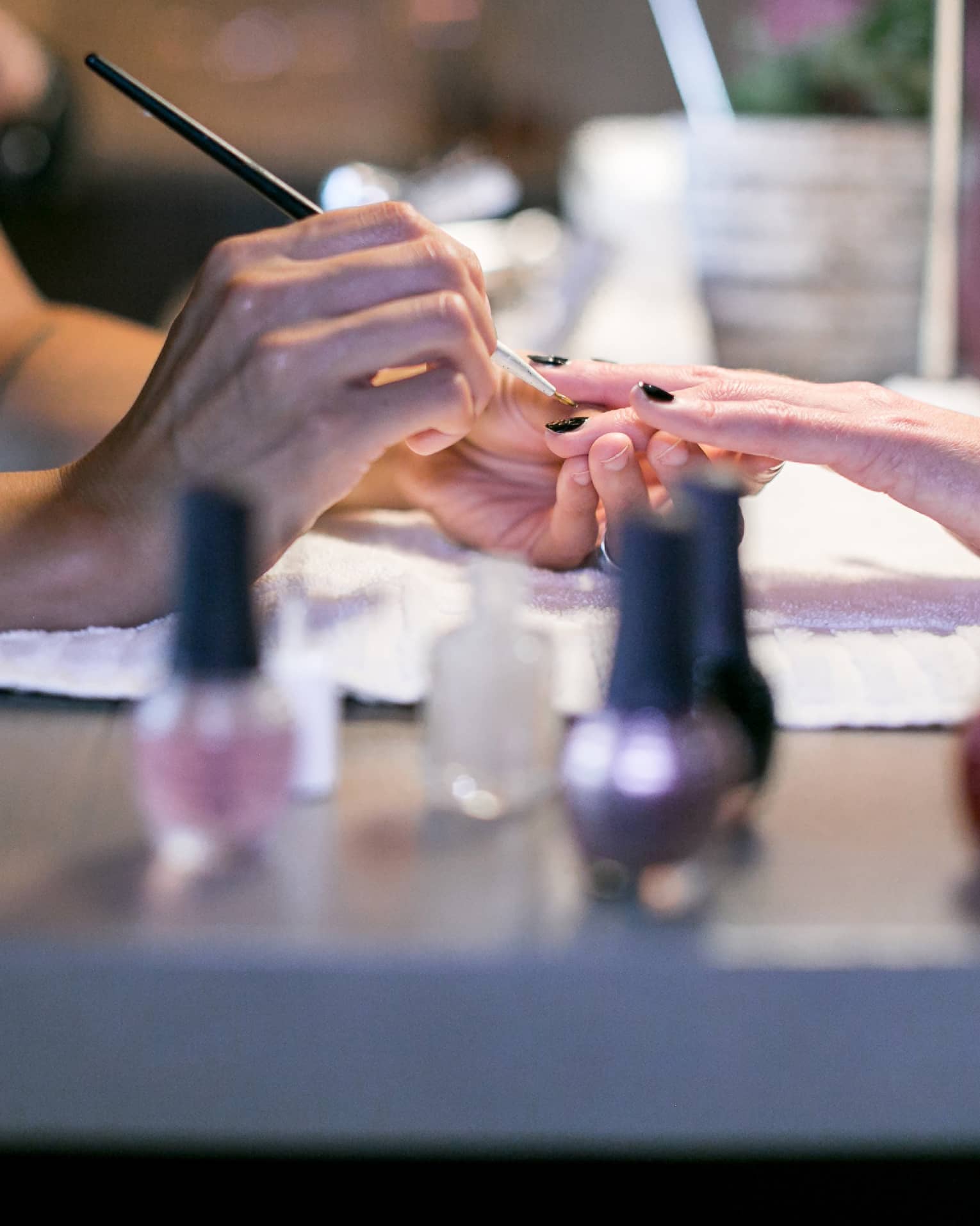 Close-up of spa staff painting woman's nails at manicure table