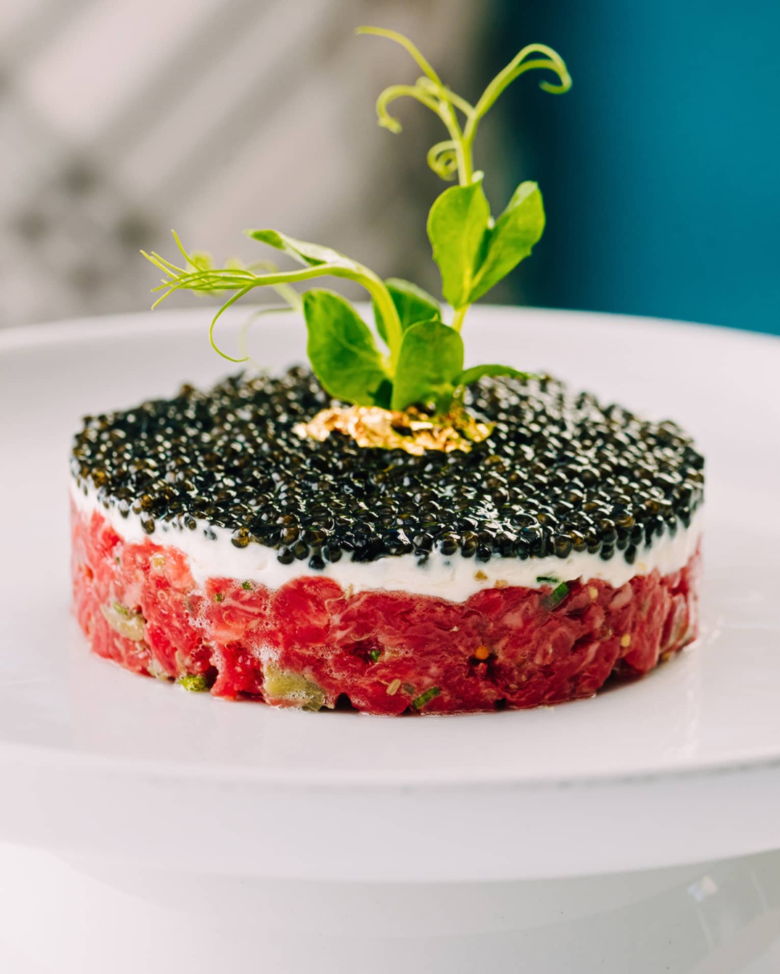 A circular tartare covered in caviar with a sprig of parsley on top. 