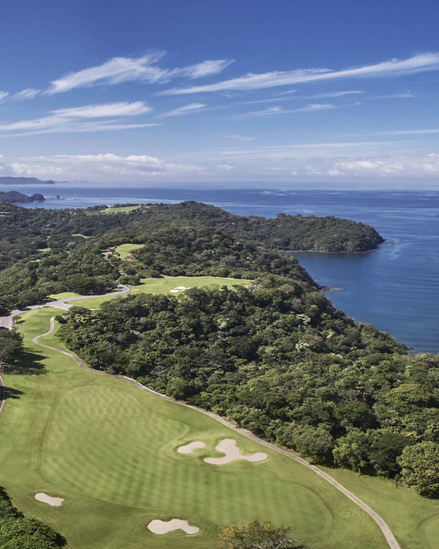 Aerial view of a golf course that stretches along a verdant peninsula by the sea