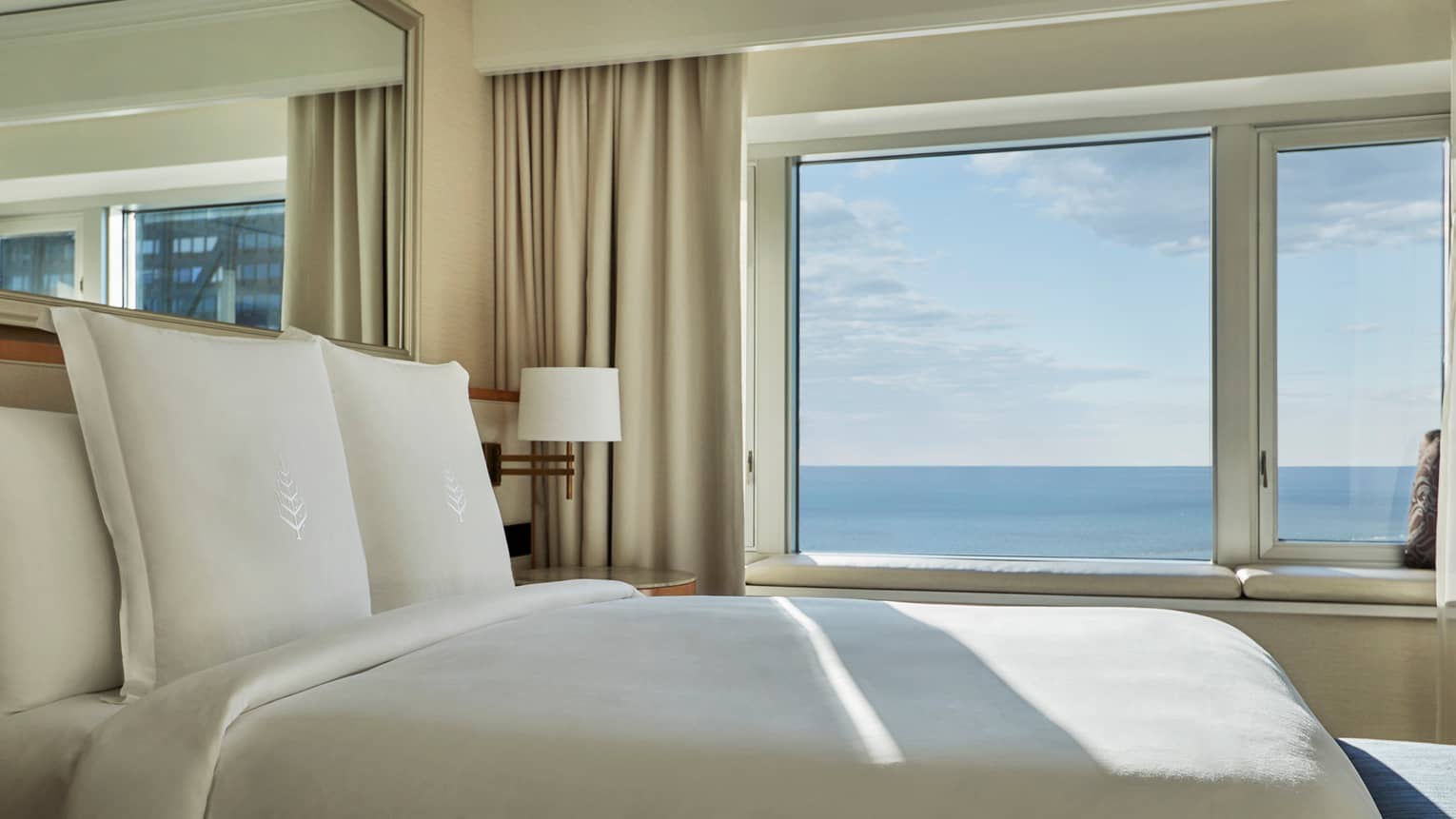 Close-up of hotel bed with white linens, Four Seasons logo by sunny window overlooking Lake Michigan