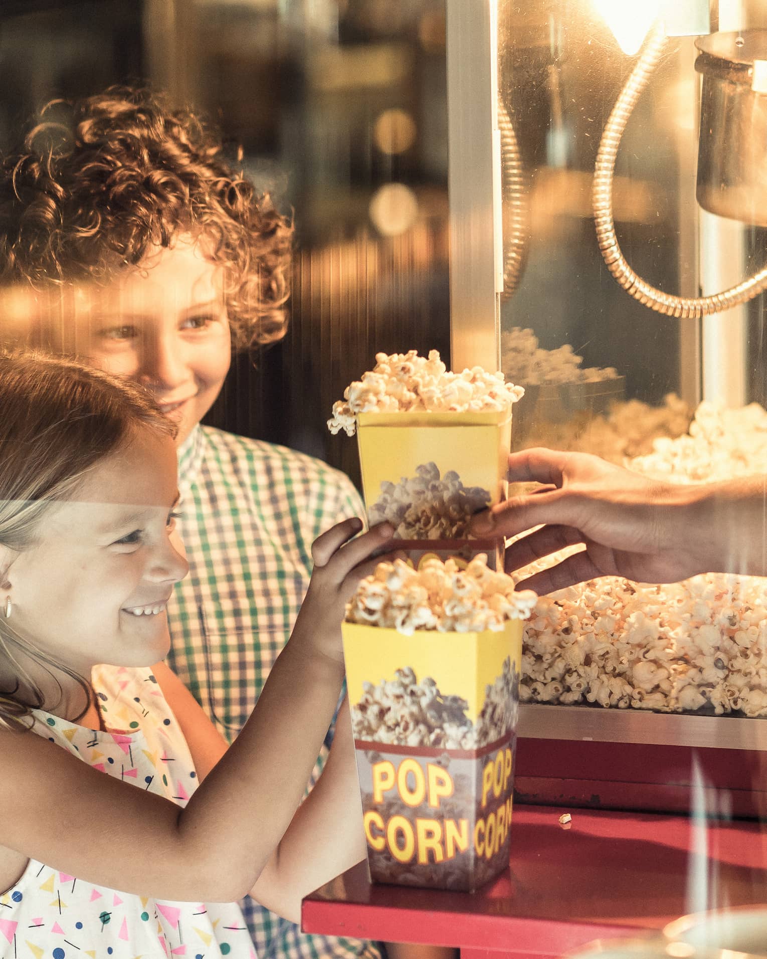 Two children smile as they wait to receive freshly popped popcorn from during BBK Brunch