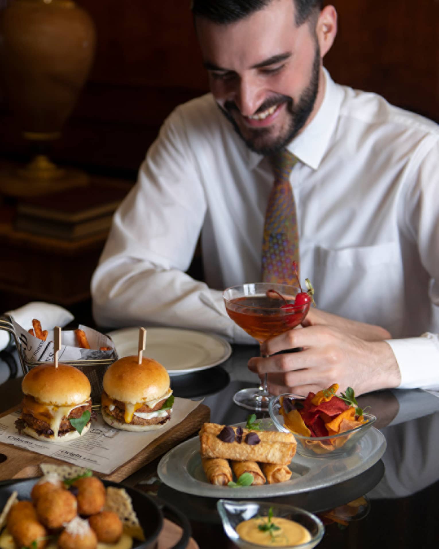 ,A couple dressed in semi-formal attire enjoys a spread of hamburger sliders, deep fried appetizers and cocktails