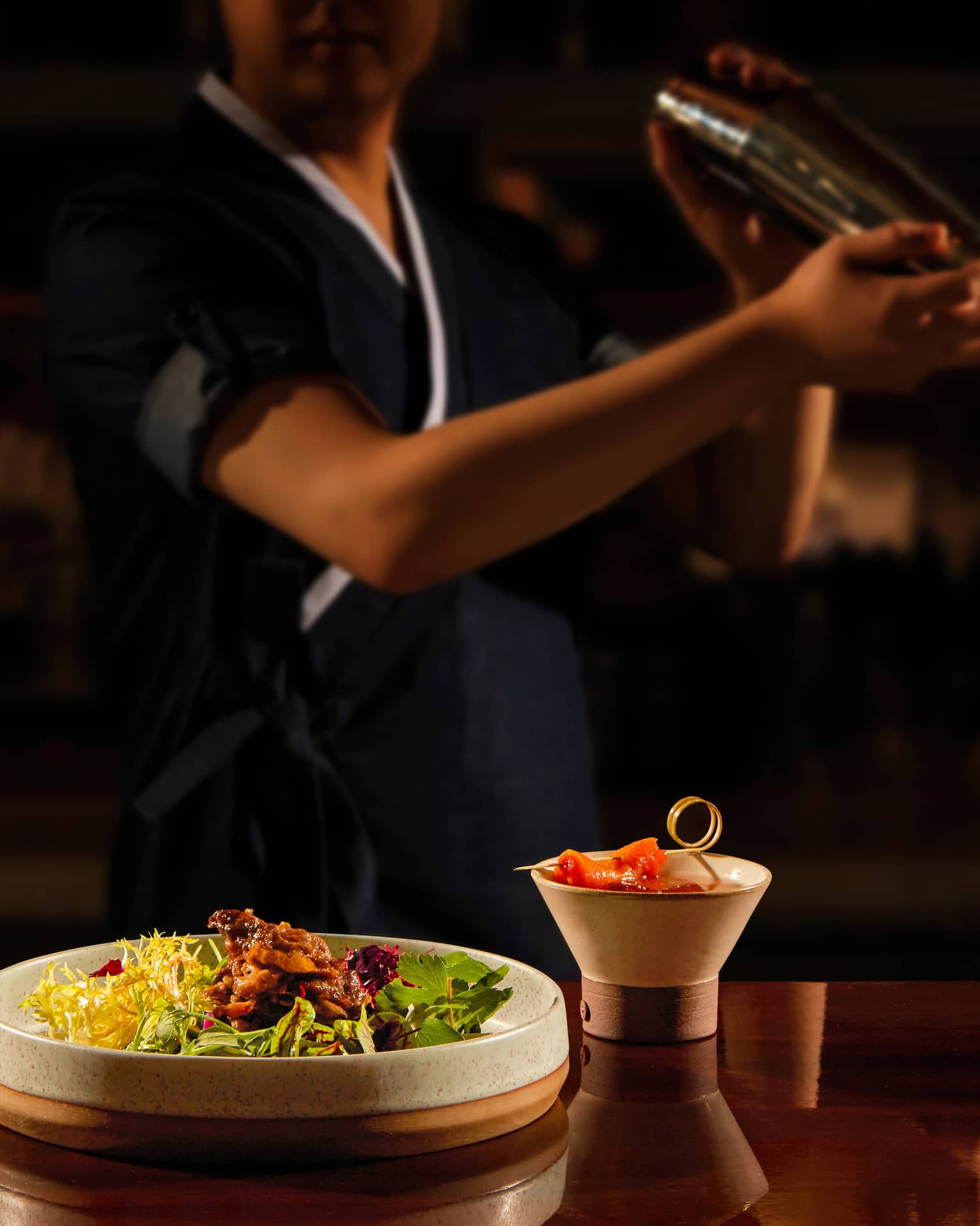 Bartender shaking a cocktail, bar bites at the forefront