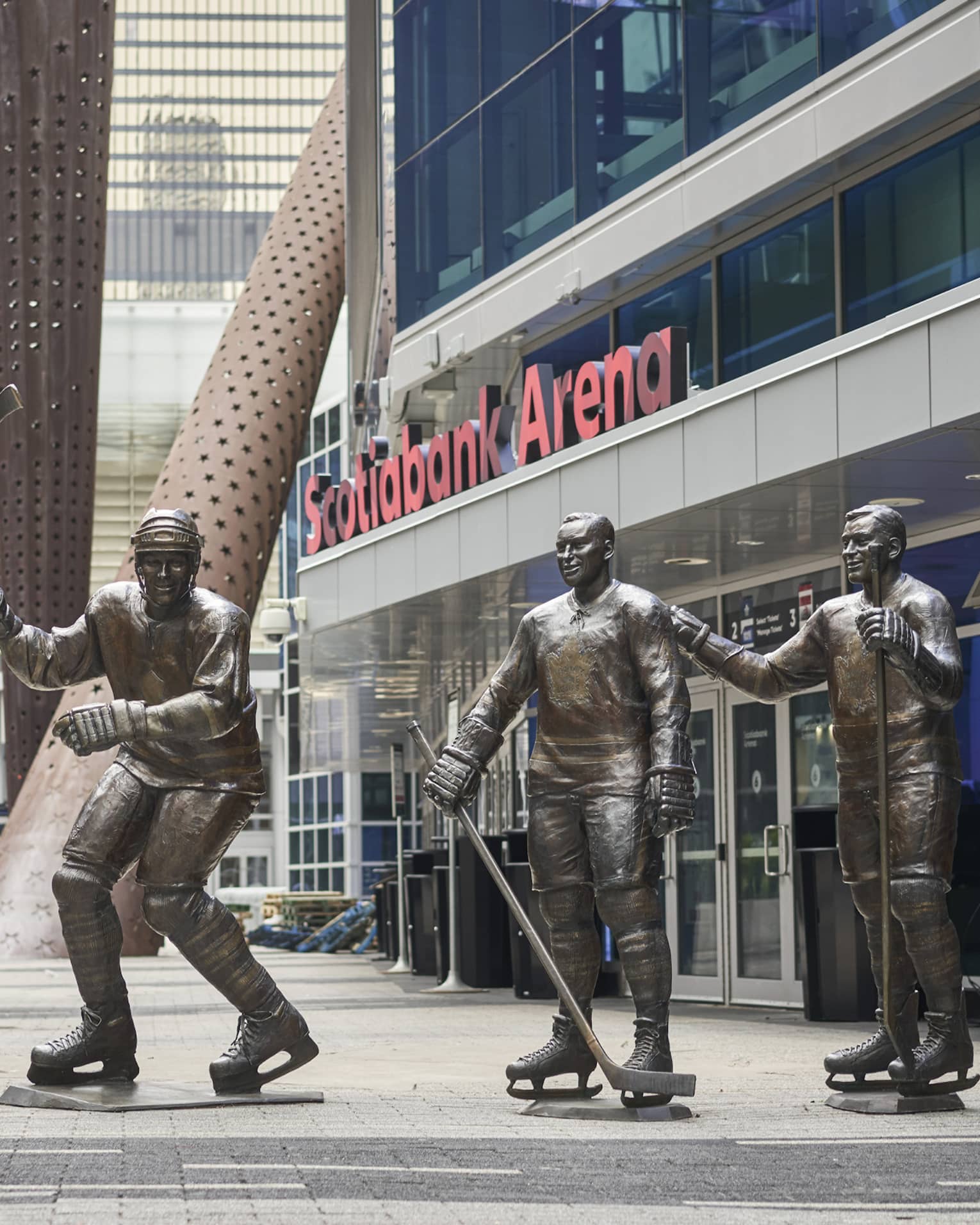 A couple walks down a sidewalk next to three bronze hockey player statues