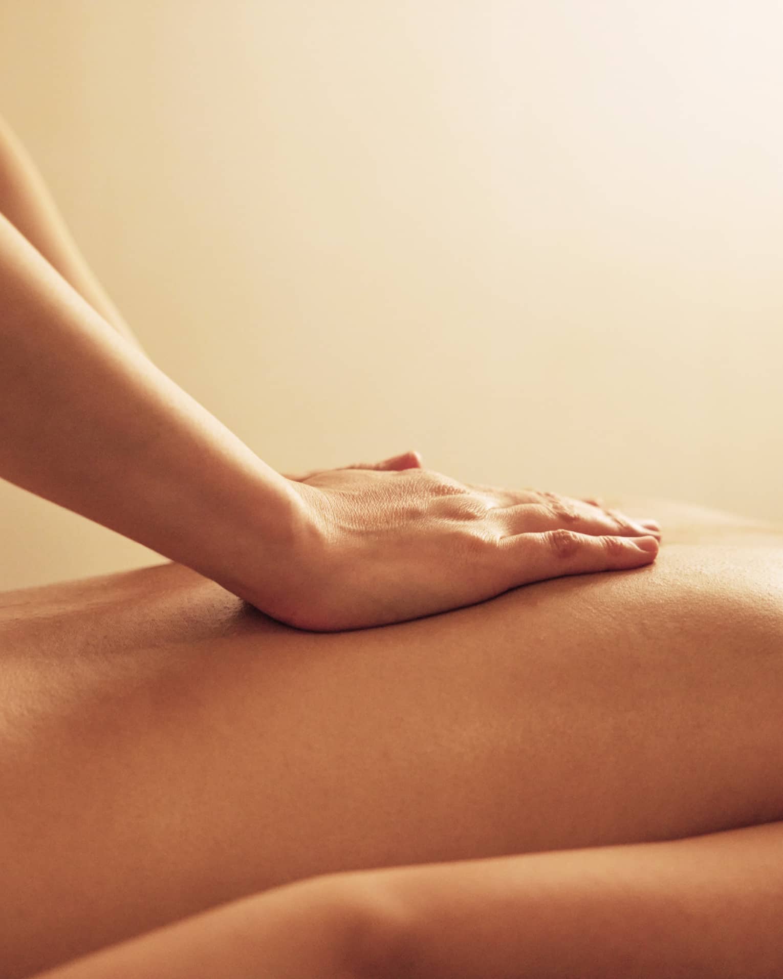 Masseuse rests hands on woman's bare back as she lays on massage table