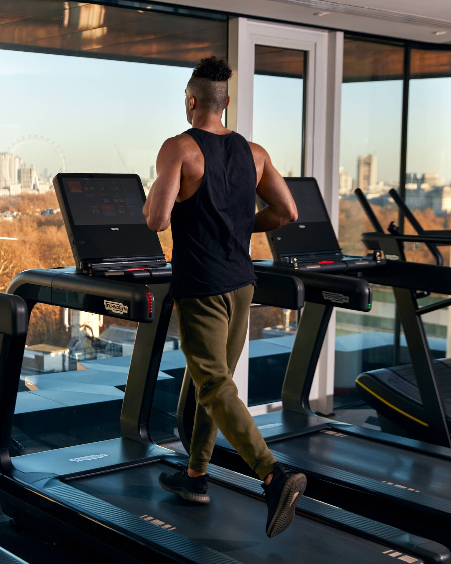 A man running on a treadmill near large windows.