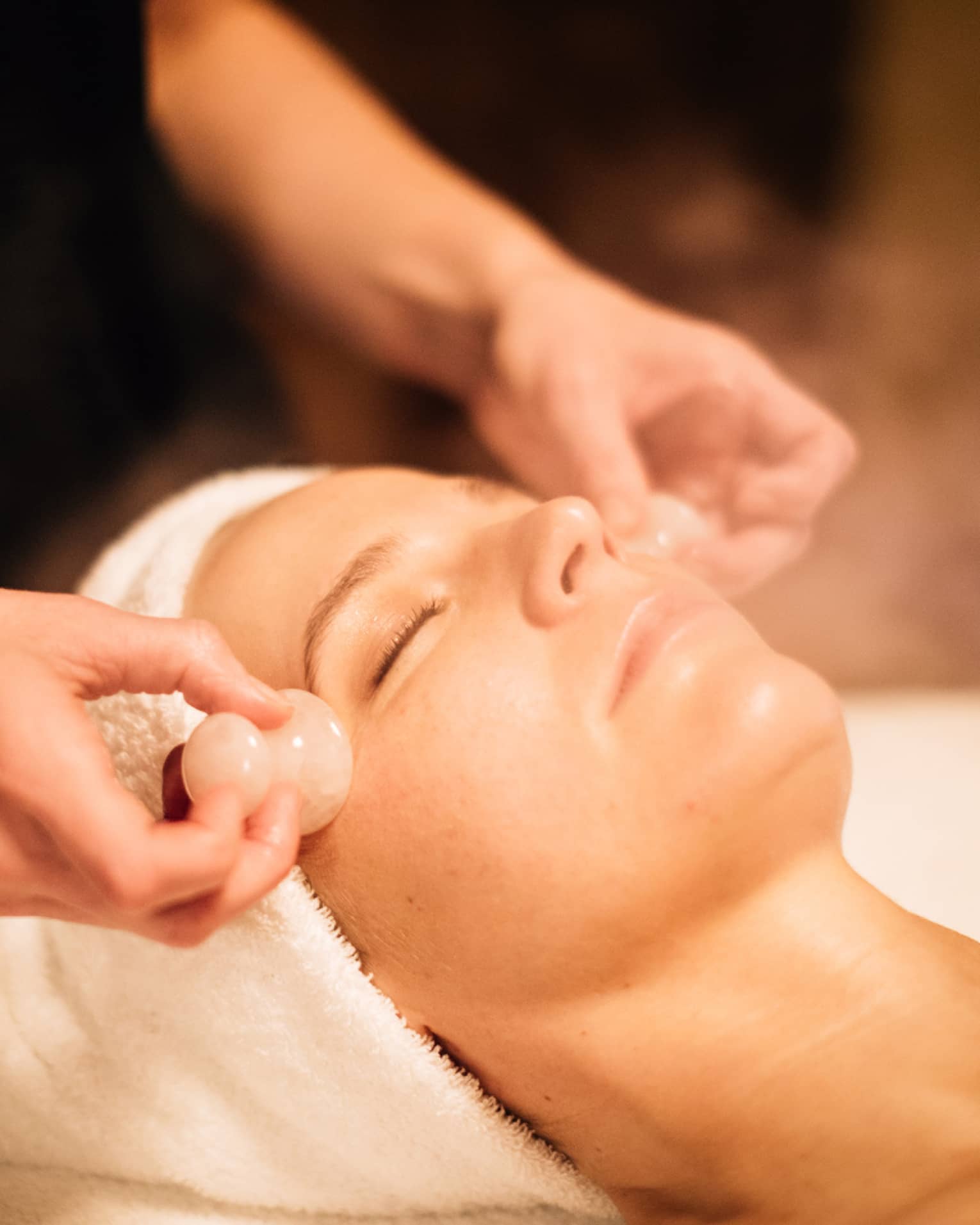 A woman receiving a facial massage with round stones.