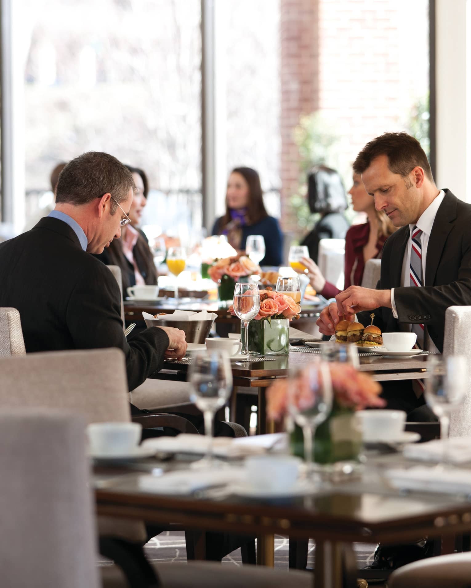 Men wearing suits dining around table in sunny Seasons restaurant, busy dining room in background