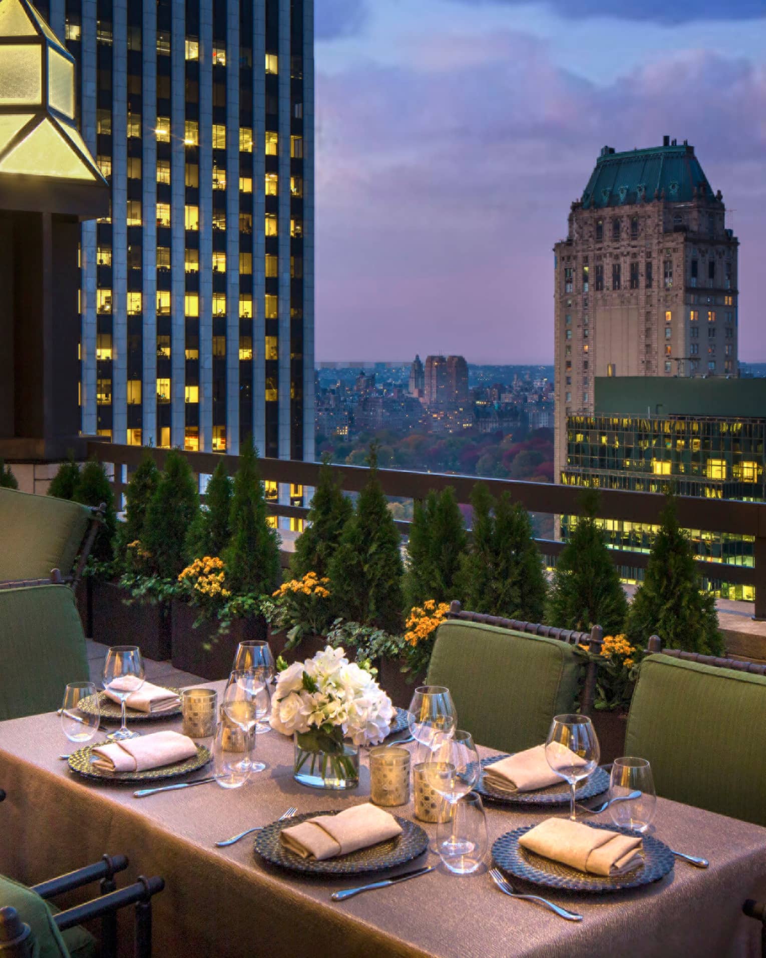 Private patio dining table with plush green cushions on chairs on rooftop terrace, city views at dusk