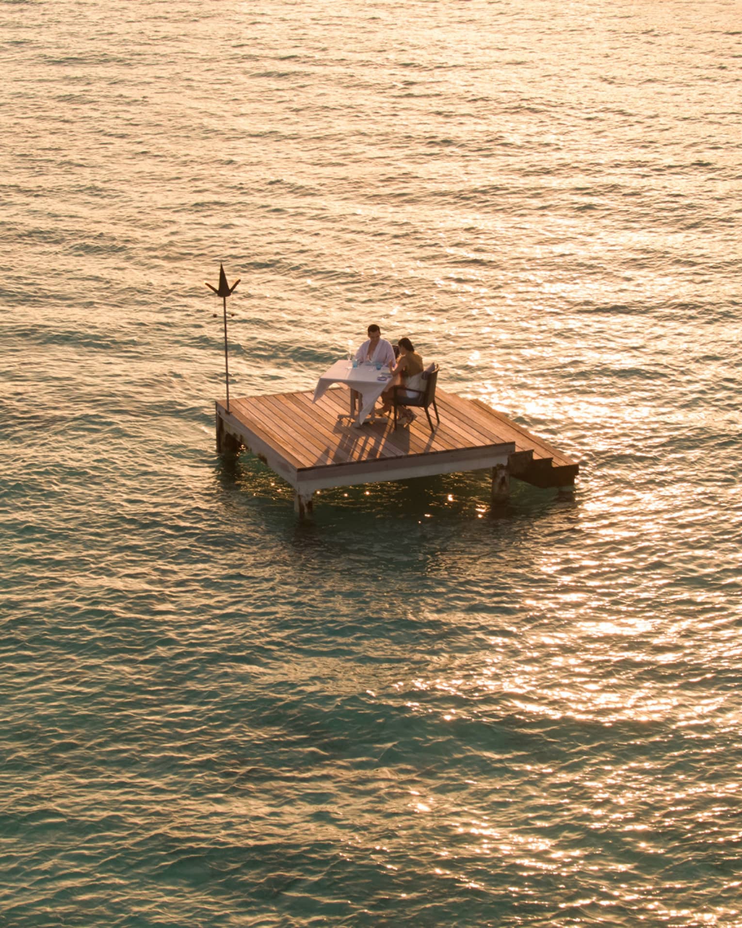 Aerial view of couple dining on small floating wood platform on moonlit lagoon