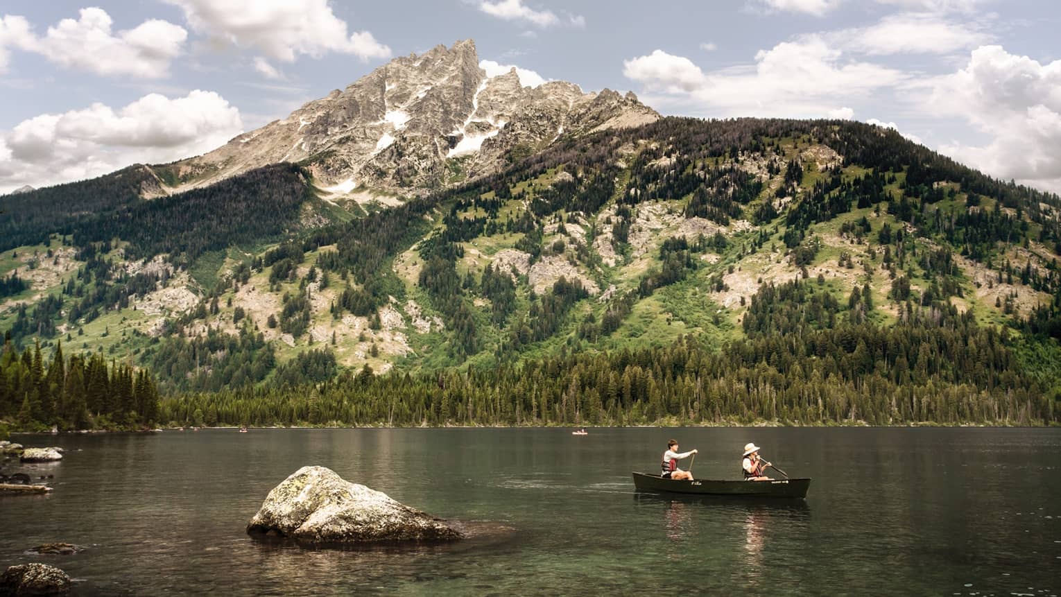 Two people in canoe on lake below towering mountains on sunny day