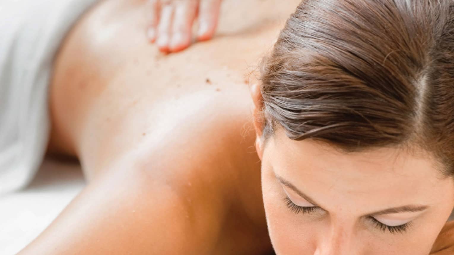 Woman closes eyes as spa staff massages her back