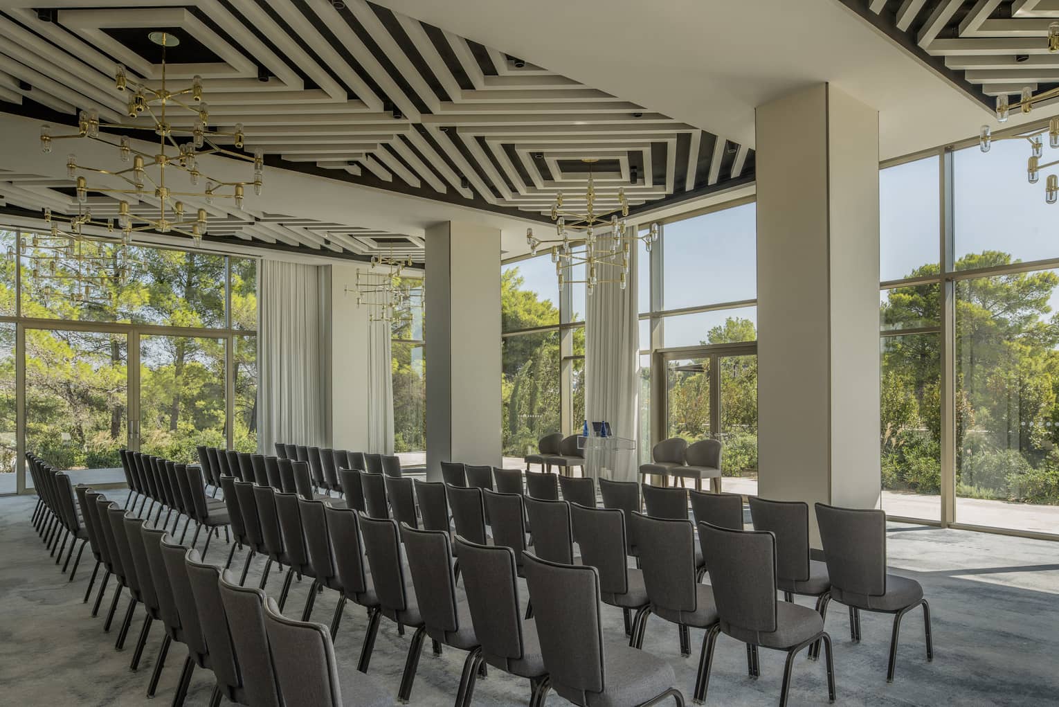 Four rows of chairs in light-filled Arion Ballroom with modern light fixtures overlooking trees