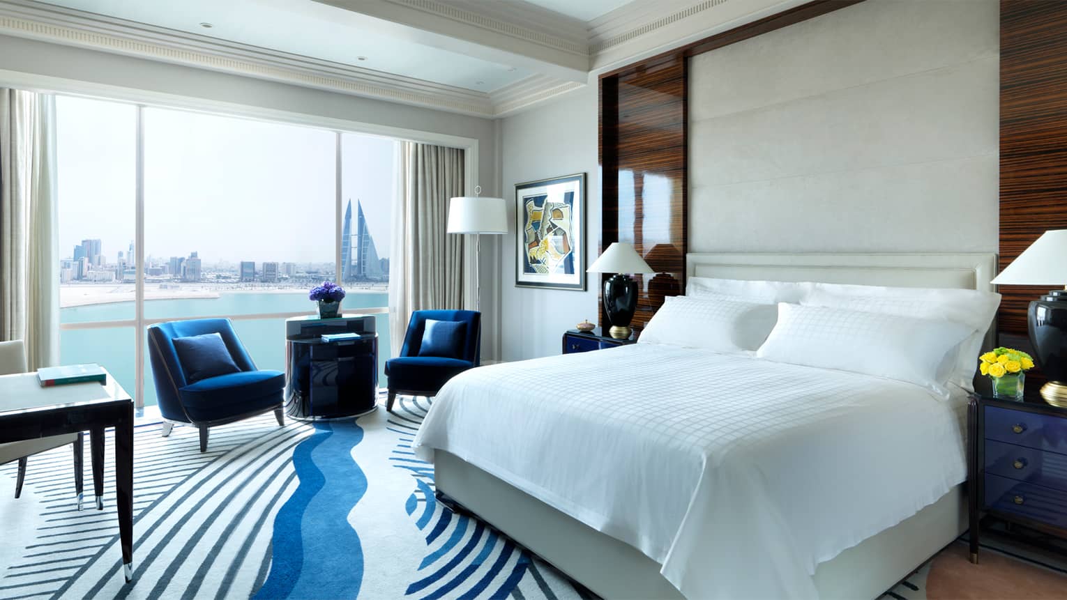 Deluxe Room bed, modern blue-and-white carpet, two blue armchairs in front of sunny windows