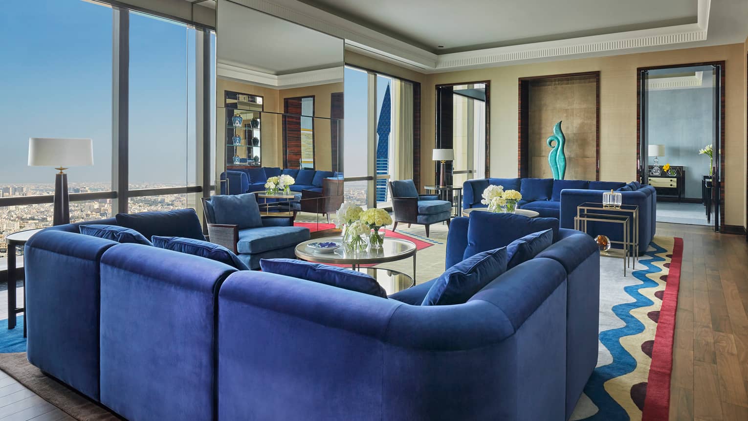 Royal Suite large u-shaped blue plush sofa, multiple seating areas, window with Bahrain city views