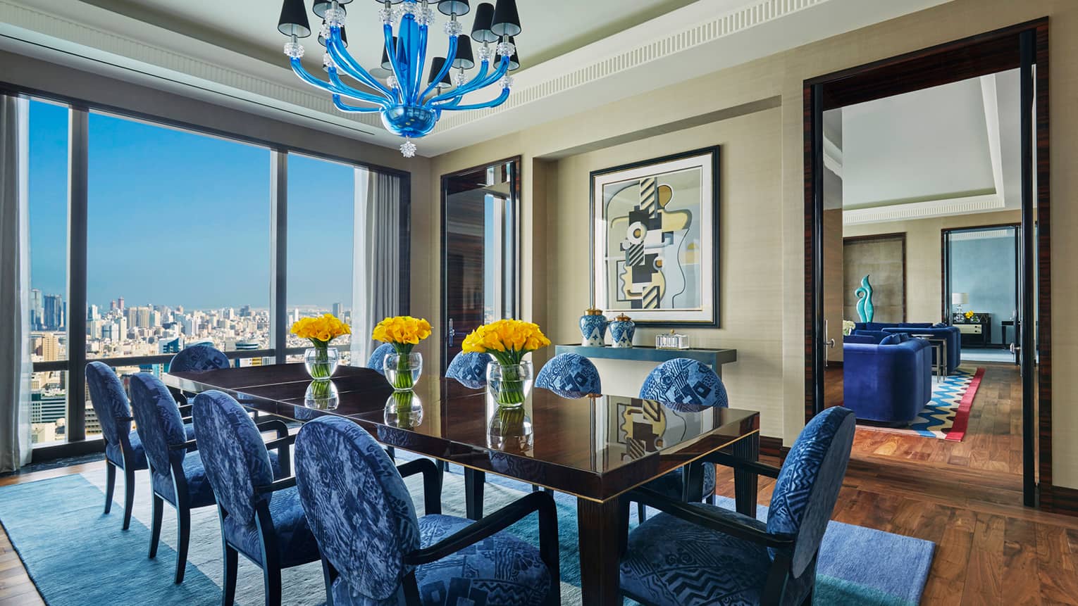 Royal Suite 10-person dining table with modern blue patterned chairs, vases of yellow flowers, blue pendant chandelier