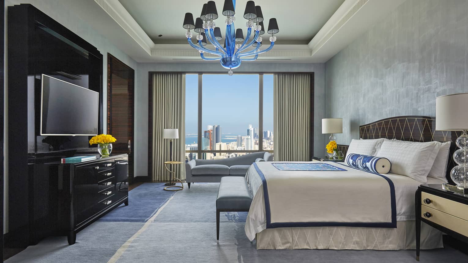 Royal Suite bed, small white bench facing dresser and TV under blue chandelier 