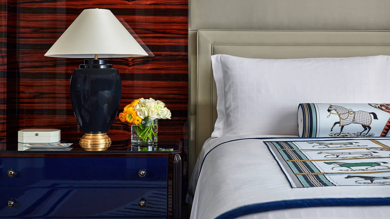 Superior Room close-up of corner of bed, pillow, decorative horse on rolled accent pillow, blue nightstand