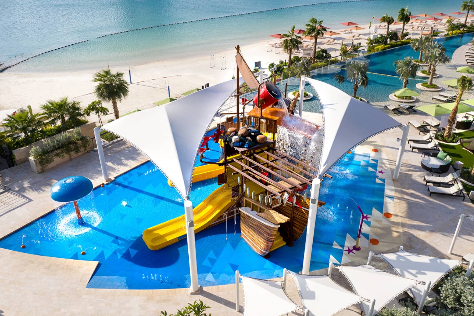 A large orange waterslide built into a faux pirate ship descending into a crystal blue pool of water.