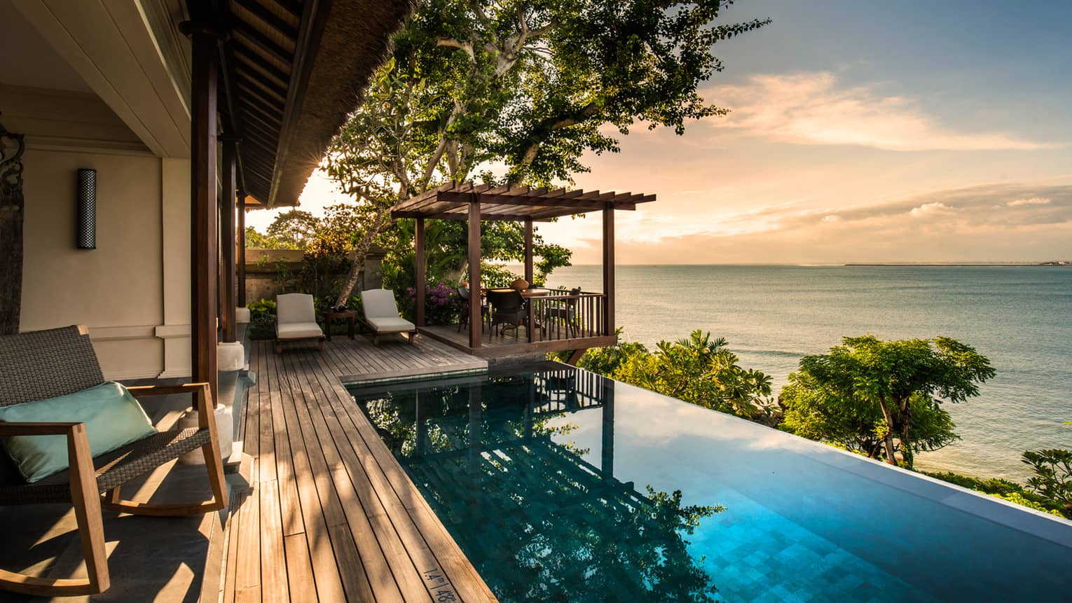 Private Ocean Villa patio at sunset with infinity swimming pool reflecting trees, clouds, white lounge chairs on side