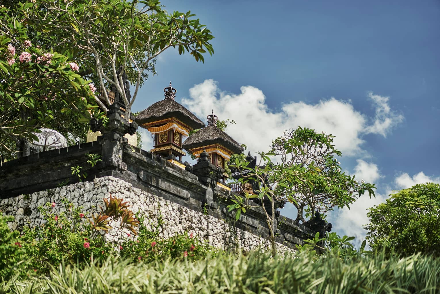 Exterior view of resort temple with stone wall, posts and carvings, tropical trees