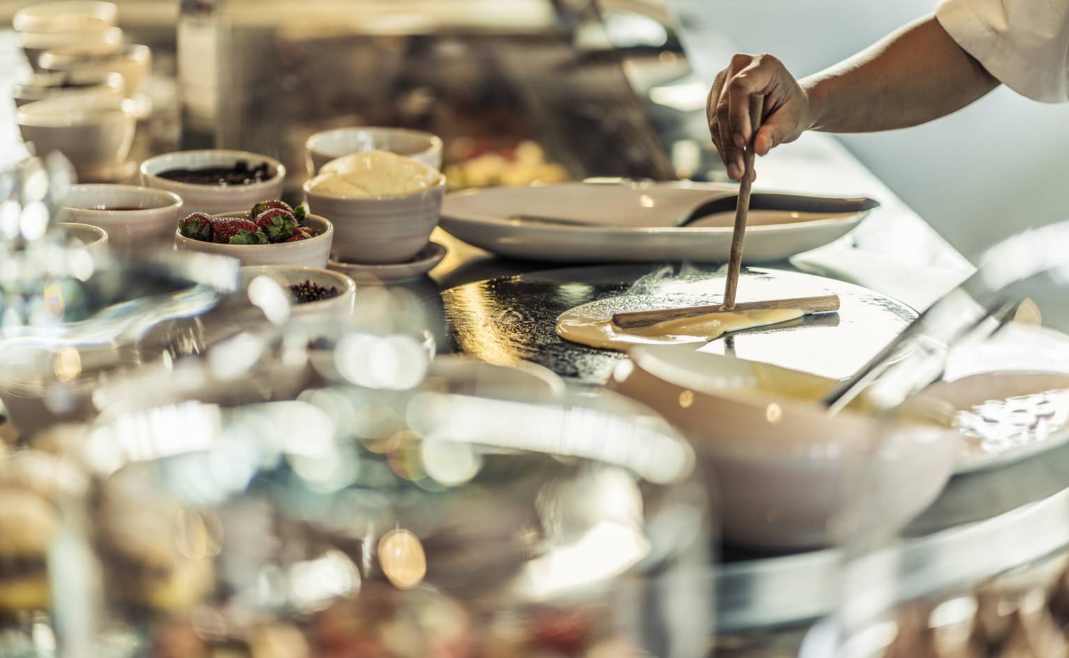 A chef pours crepe batter onto a hot plate near the crepe buffet