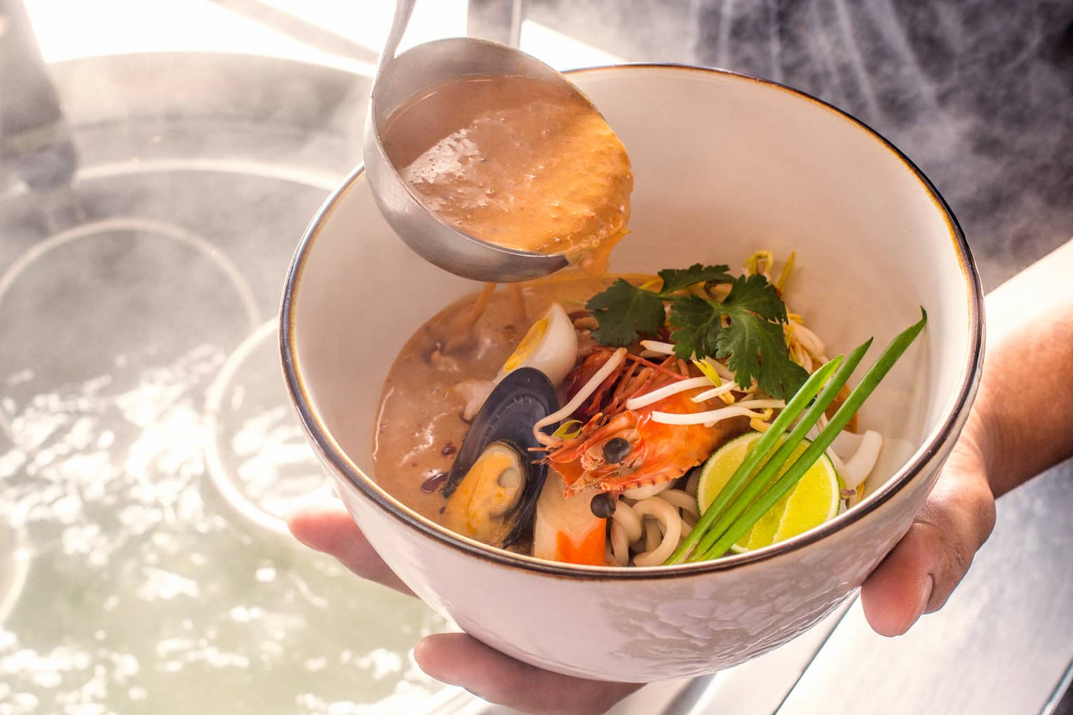 Close-up of hands holding Laksa Noodle seafood dish, ladle with sauce 