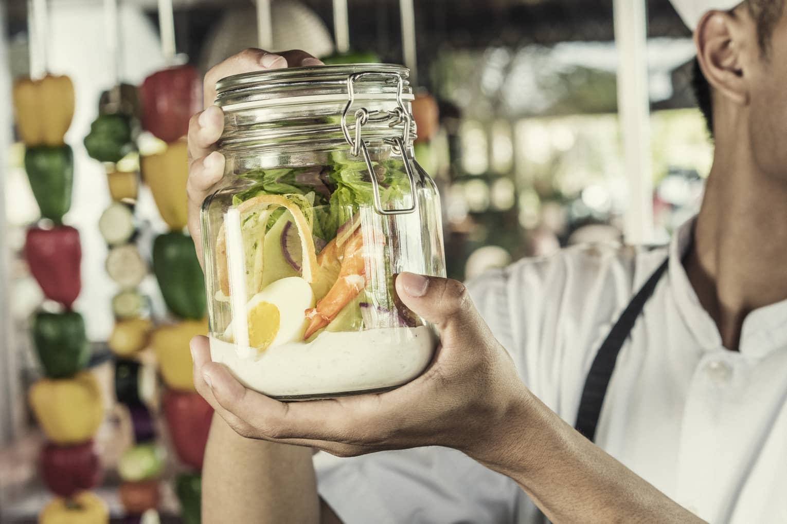 A chef shakes a caesar salad in a glass jar with some dressing