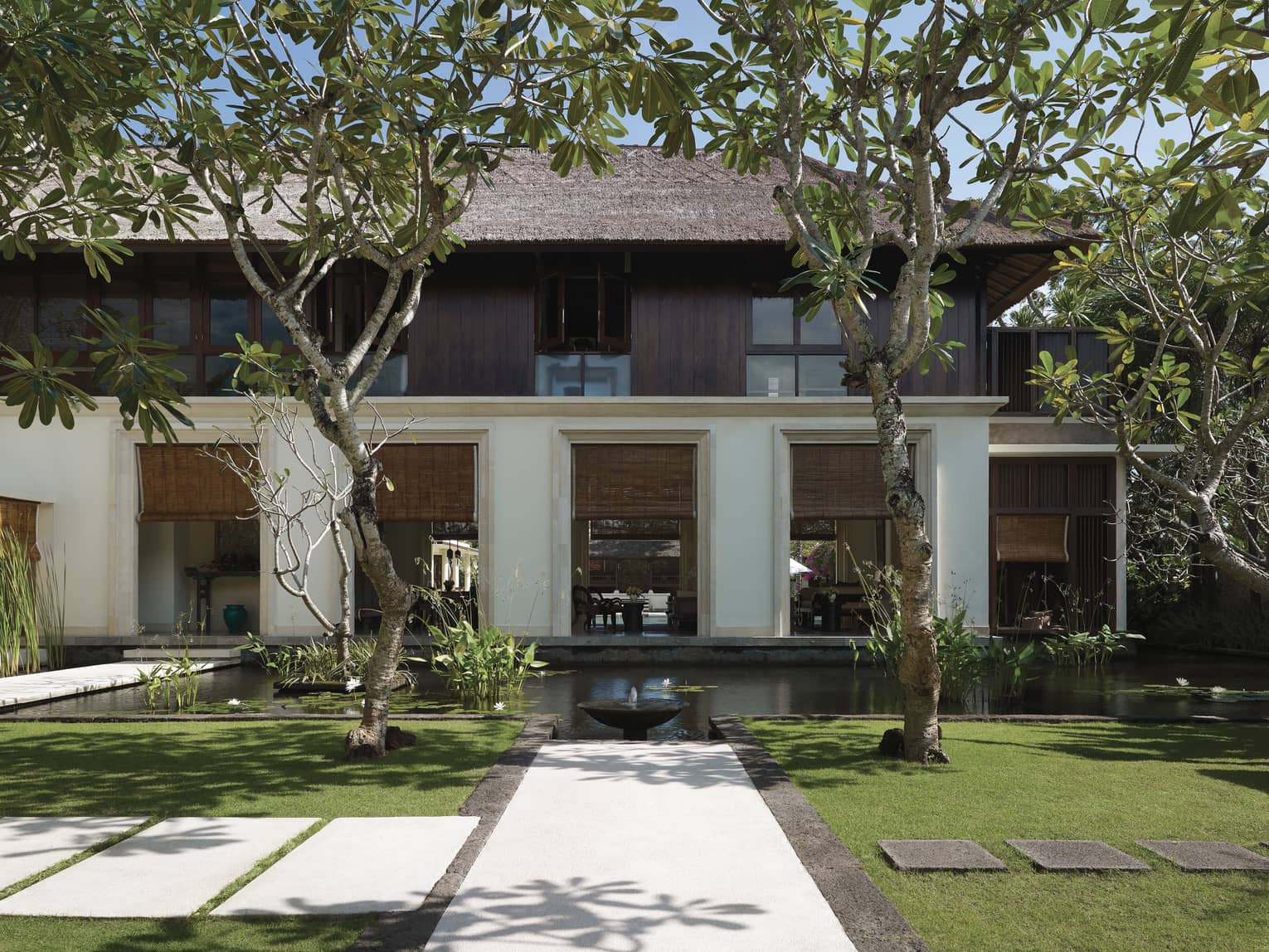 Exterior villa view with pond, small fountain, manicured green lawn, tropical trees