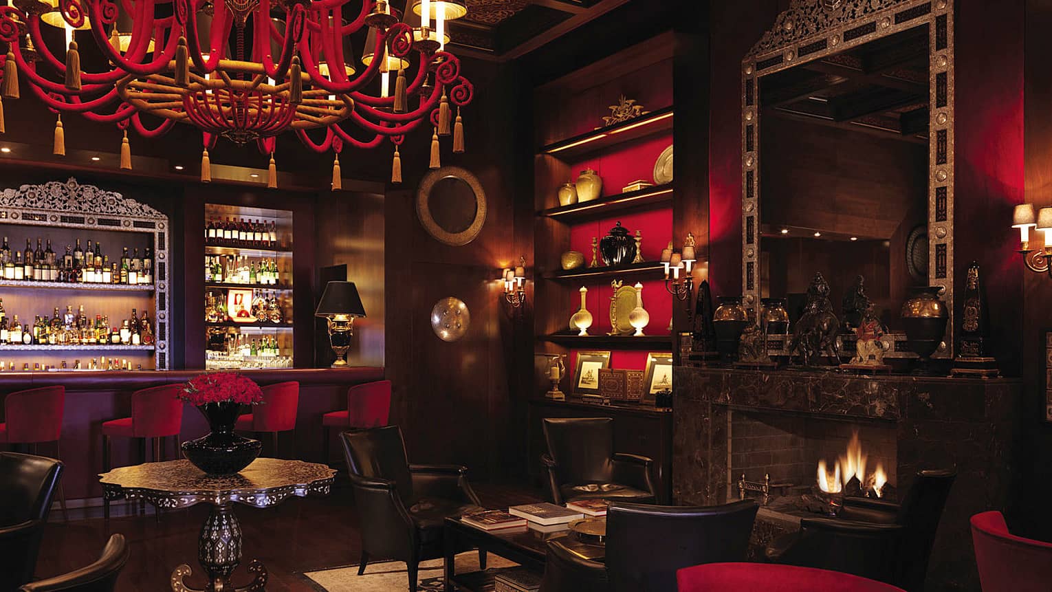 Bar interior with dark wood, red chandelier, shelf and velvet bar stools, arabesque ceiling, fireplace