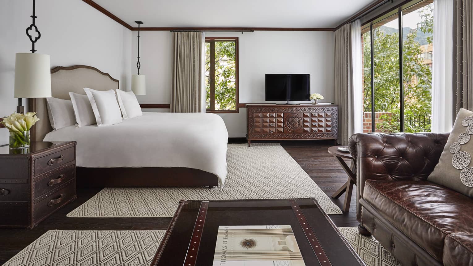 Executive Suite with bed with white linens, wood trunk-style coffee table and nightstand, large glass patio door