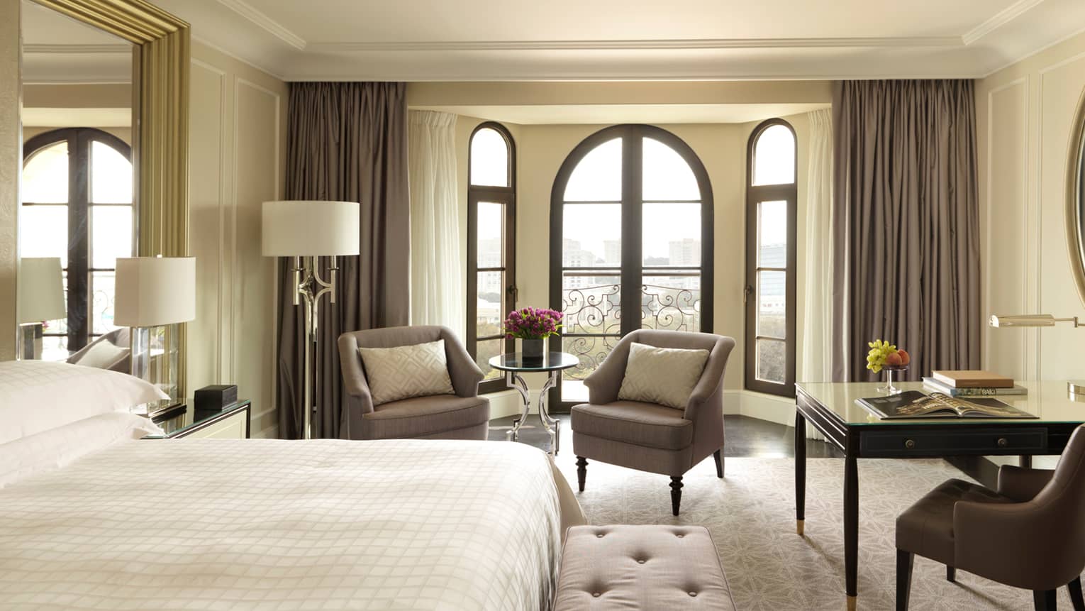 Sunny Deluxe Caspian Room hotel room with arched French doors, two armchairs, desk, bed