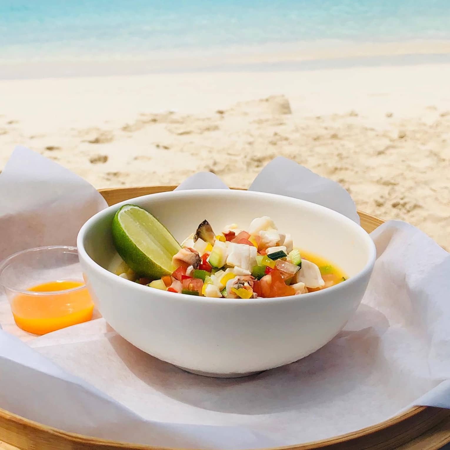 Fresh ceviche served in a white bowl with a lime wedge on the side, overlooking a sandy beach and turquoise ocean