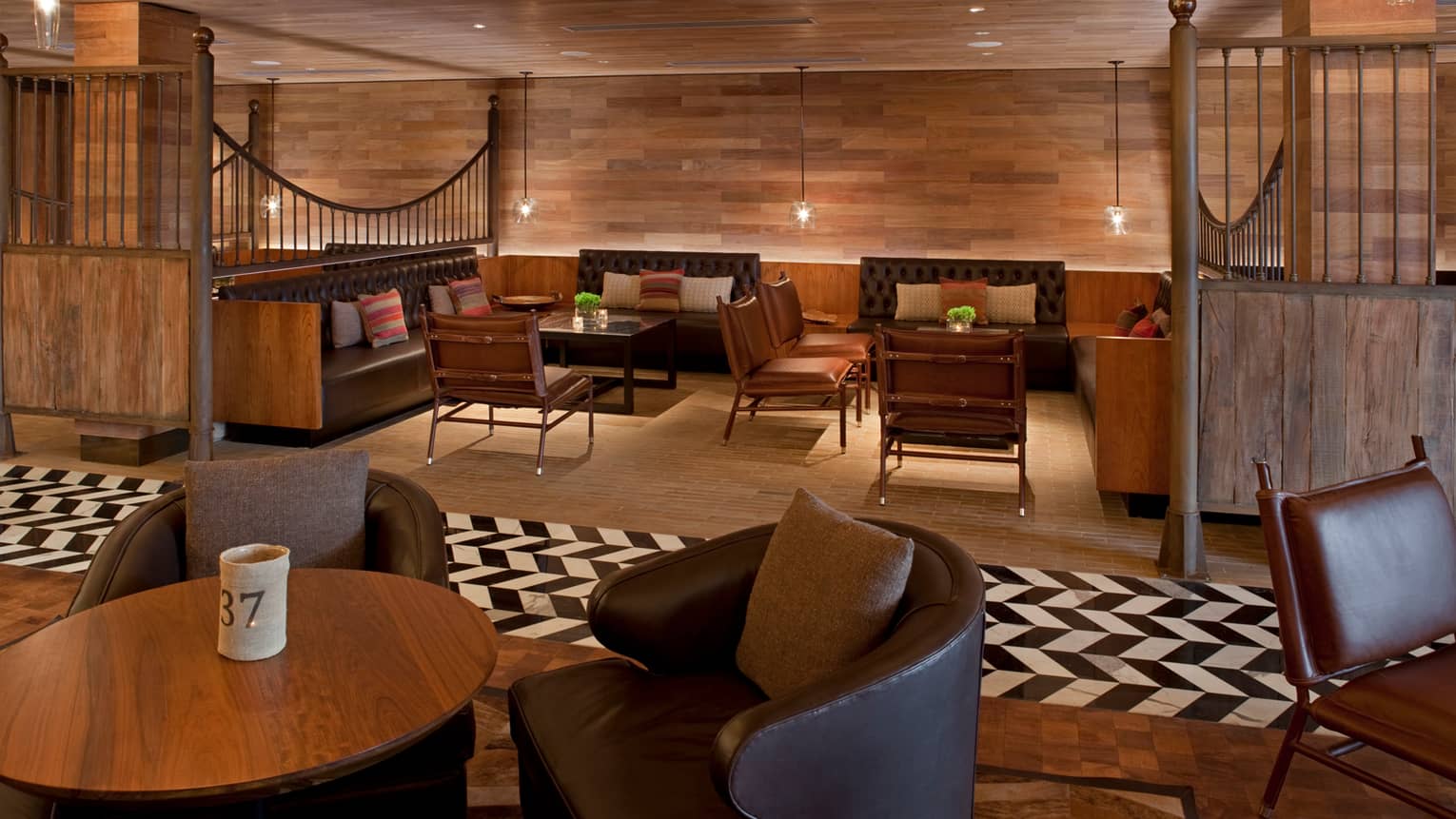 Pony Line lounge with rich brown wood flooring and walls over tables with stools, leather chairs, glass lamps
