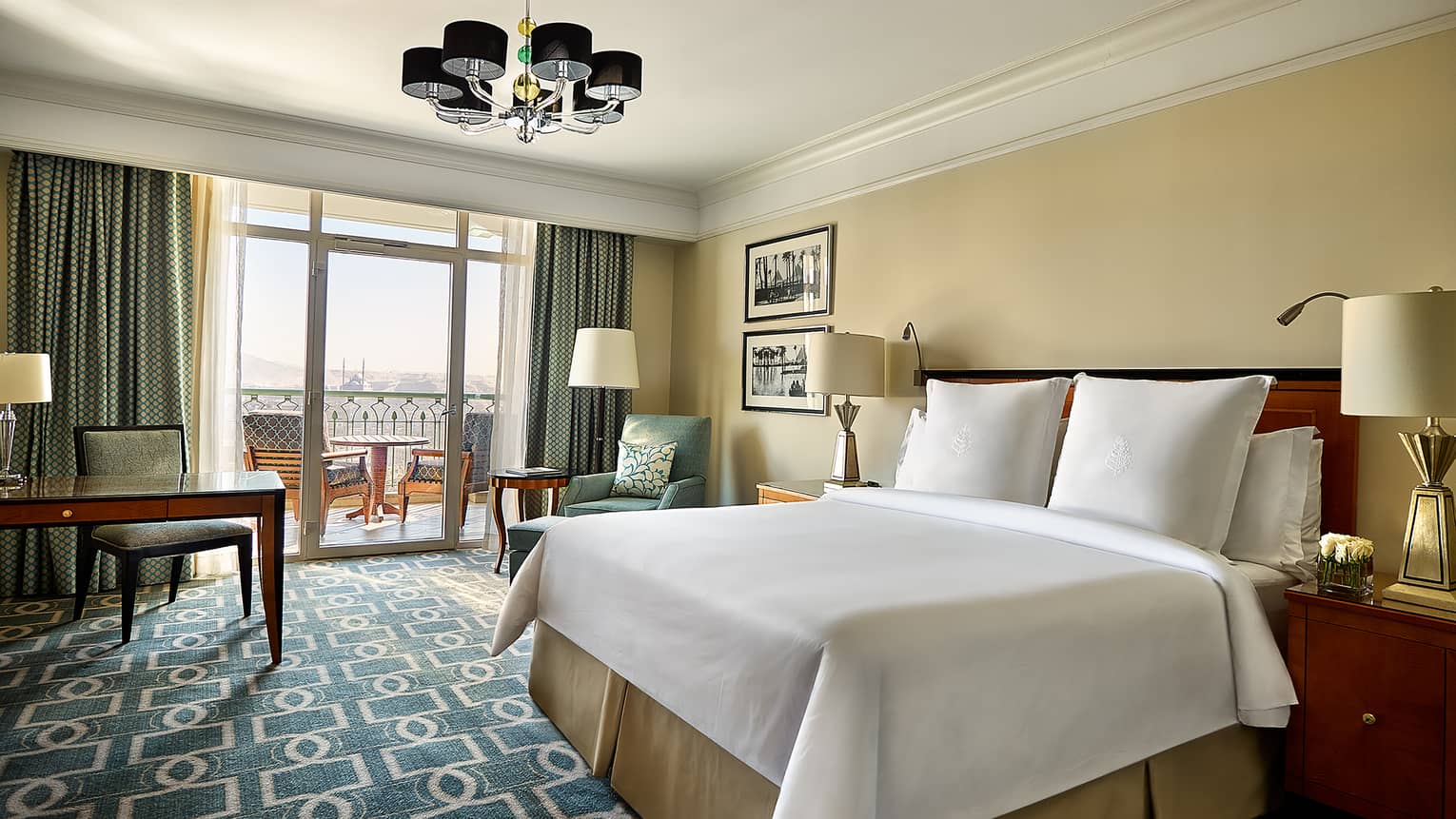 Deluxe Room white bed with green-and-white patterned carpet, desk, green chair and curtains and balcony doors